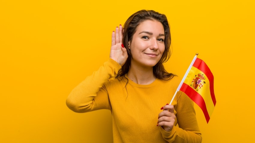 Jeune fille portant un drapeau espagnol et faisaint mine d'écouter en mettant une main dérrière son oreille 